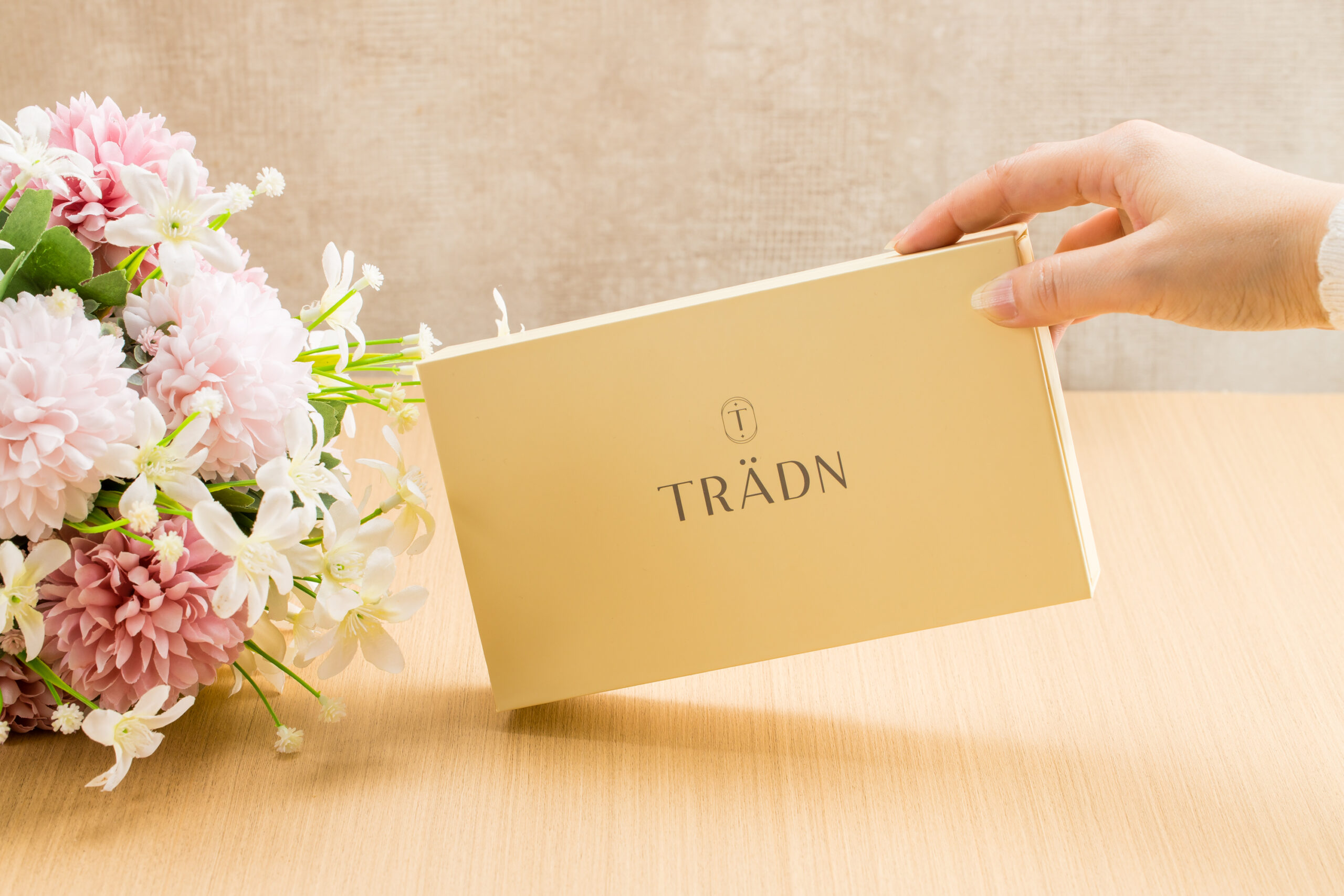 Hand holding the TRÄDN Essential Oils Gift Set box beside flowers on a wooden table.